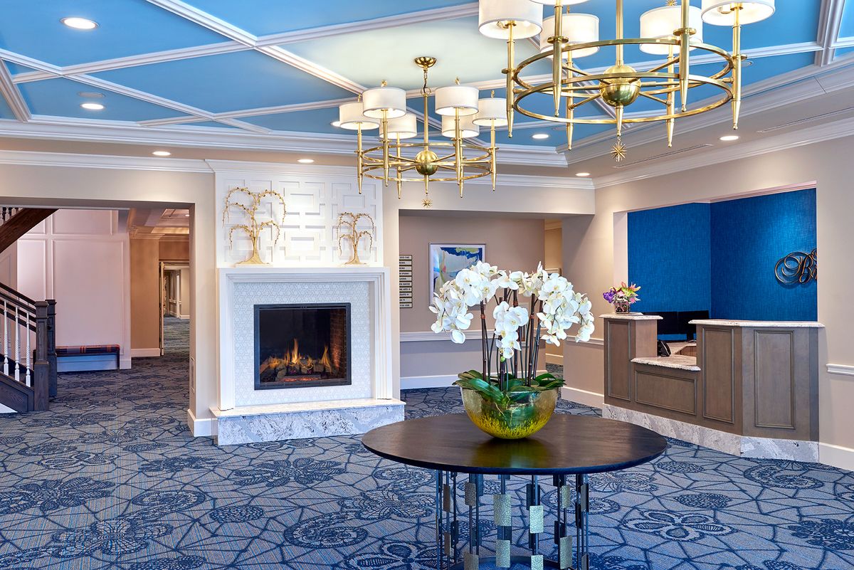 A luxurious hotel lobby featuring a fireplace, elegant chandeliers, and a central table with orchids.