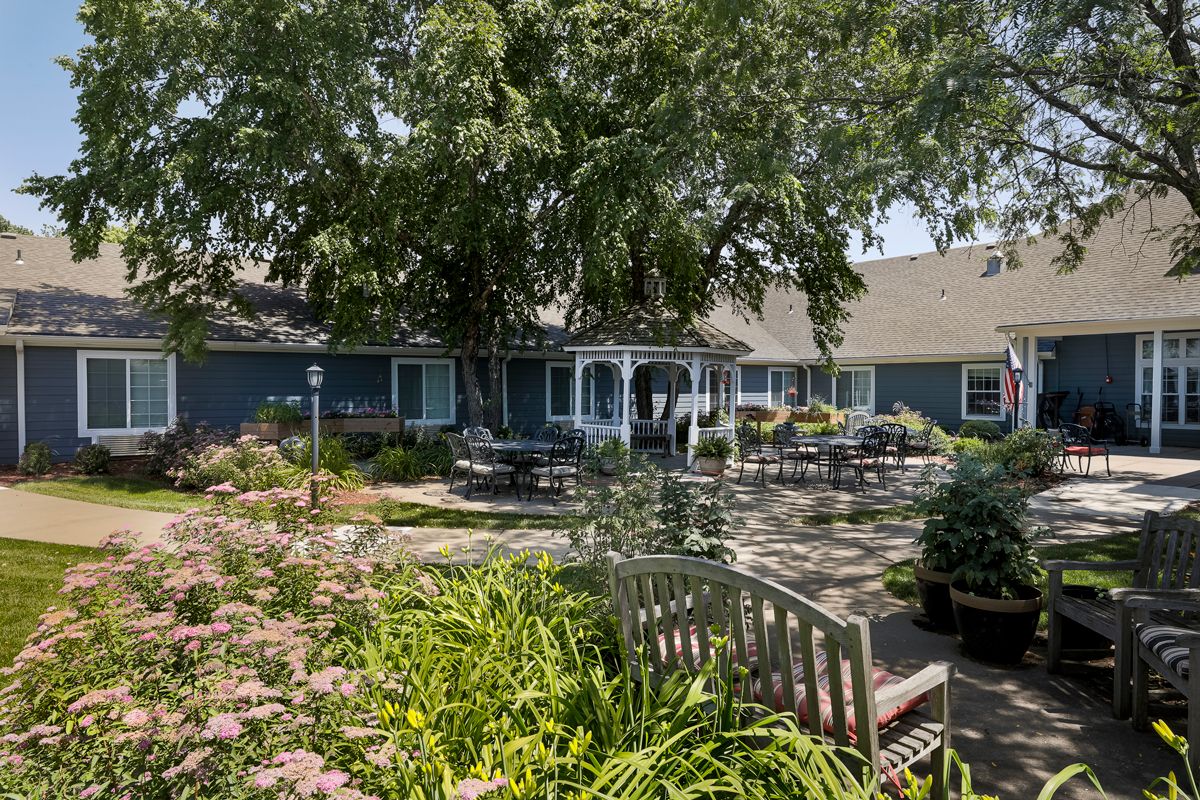 A serene garden with lush greenery and outdoor seating in front of a blue house.