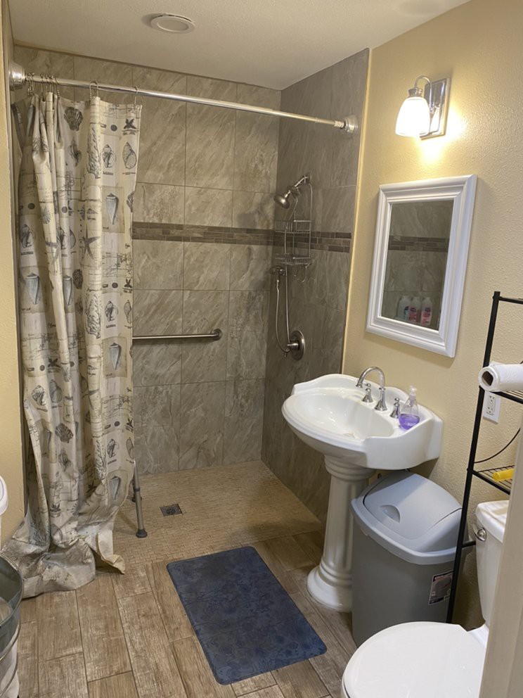 A clean and organized bathroom with a shower, sink, and mirror under a light.