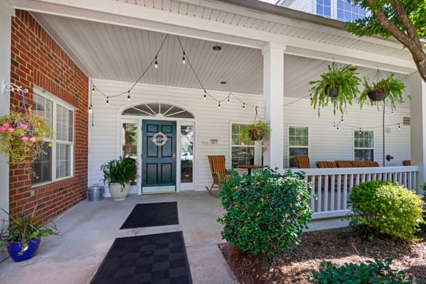 A welcoming porch with a blue door, string lights, and outdoor seating surrounded by greenery.