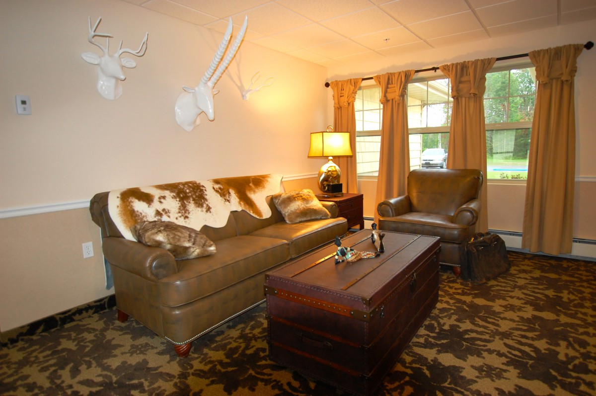 A cozy living room with a leather sofa, armchair, and decorative animal heads on the wall.