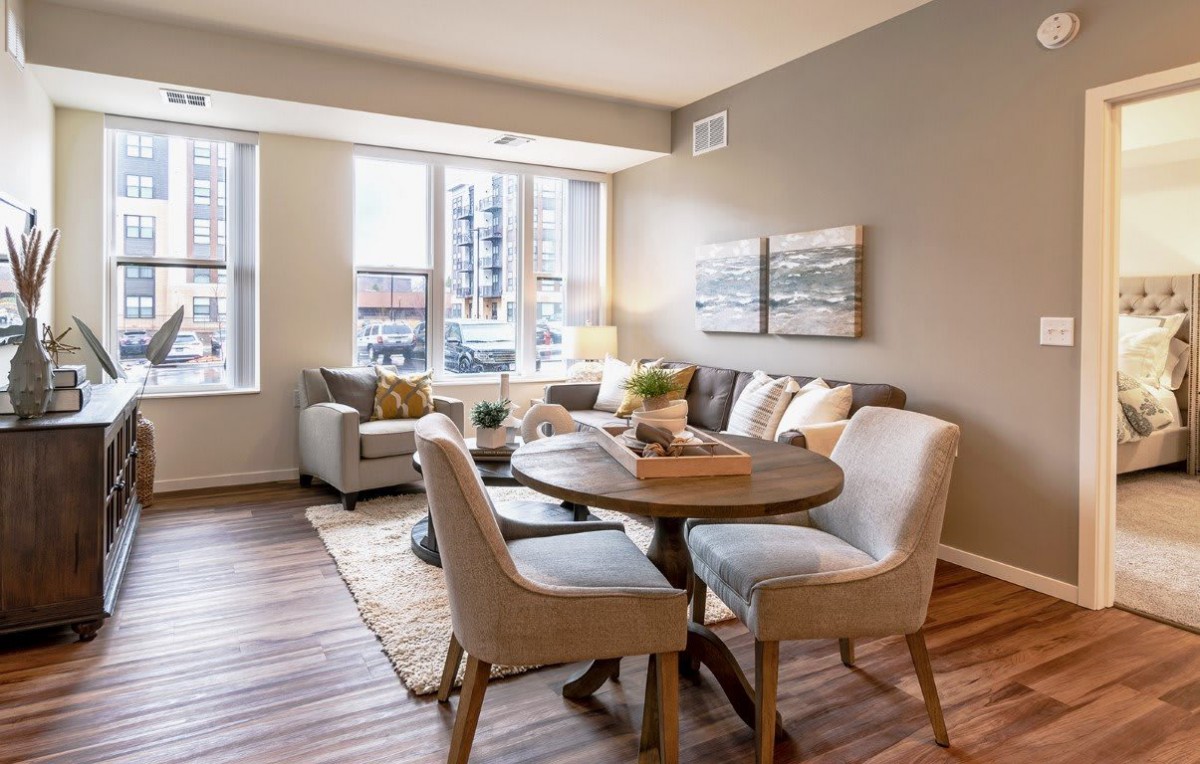 A modern living and dining area with ample natural light, featuring stylish furniture and wood flooring.