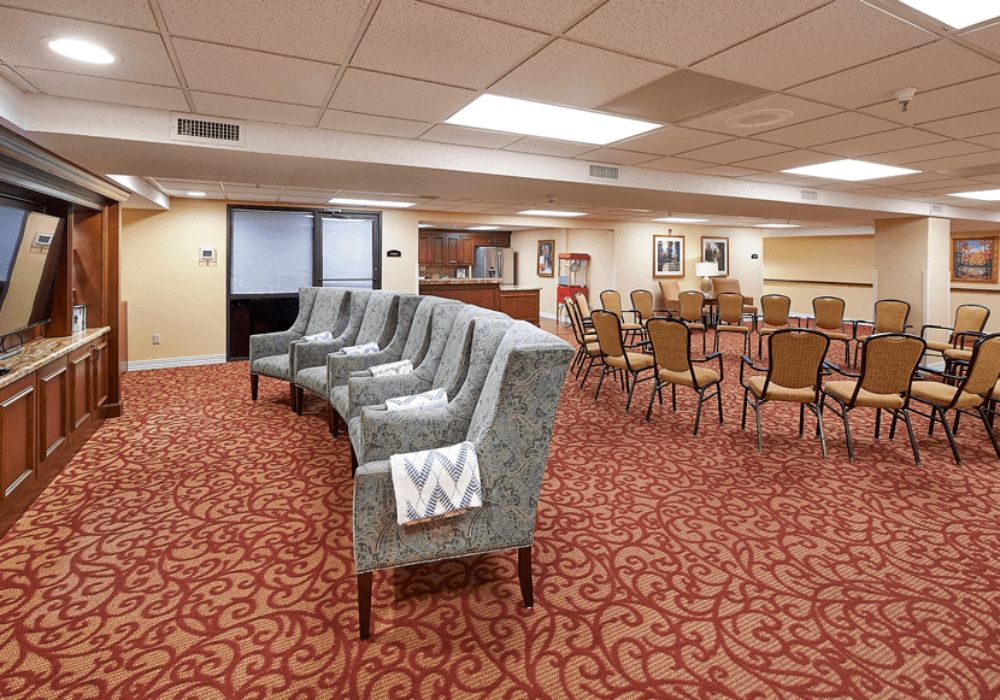 A spacious conference room with upholstered chairs and red patterned carpeting.