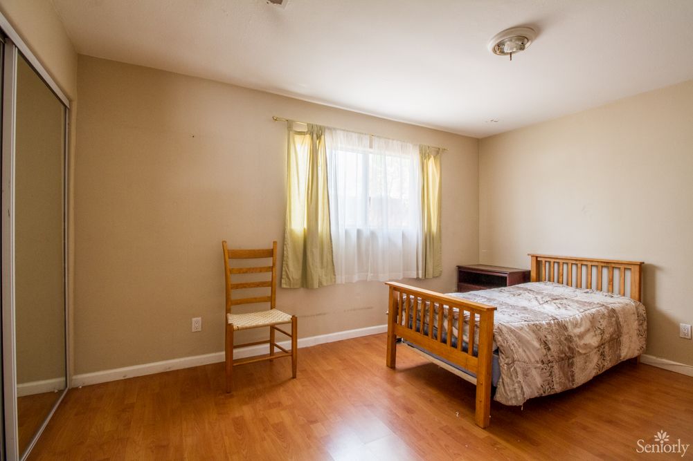 A minimalist bedroom with a bed and a chair next to a window with light curtains.