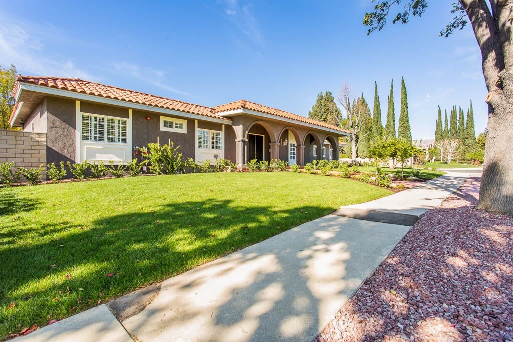 A spacious suburban house with a well-maintained front lawn and surrounding greenery on a sunny day.