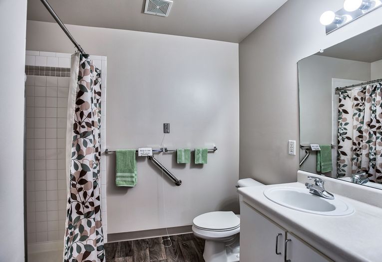 A modern bathroom featuring a shower with a patterned curtain, a toilet, and a sink with a mirror above it. Green towels are neatly hung on the towel rack.