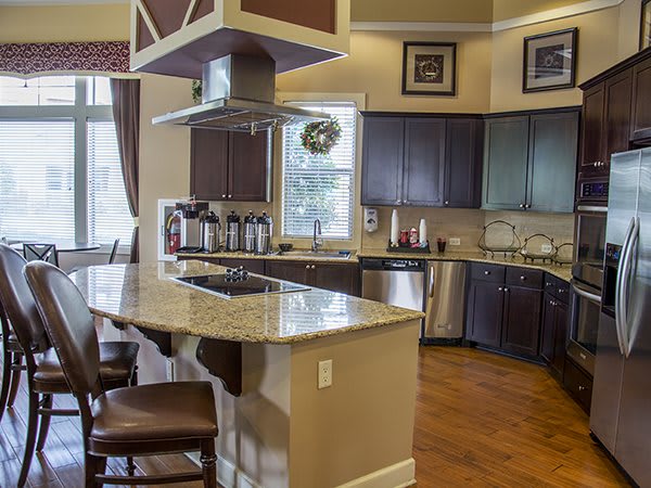 A modern kitchen featuring a central island with granite countertops, dark wood cabinetry, and stainless steel appliances.