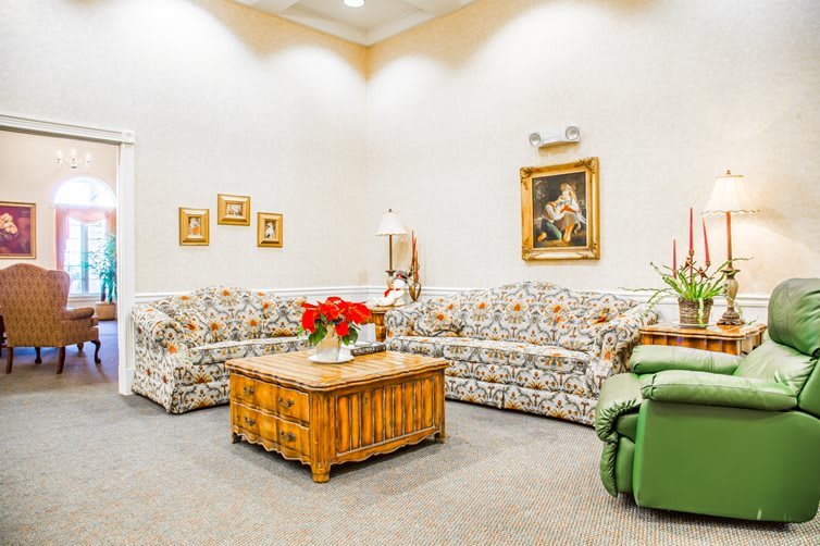 A cozy living room with floral-patterned sofas, a wooden coffee table adorned with a flower arrangement, and artwork decorating the walls.