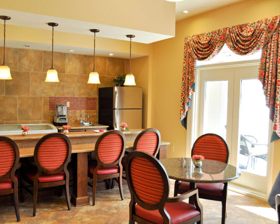 A cozy dining area with red upholstered chairs and a kitchen counter, featuring pendant lighting and a refrigerator.
