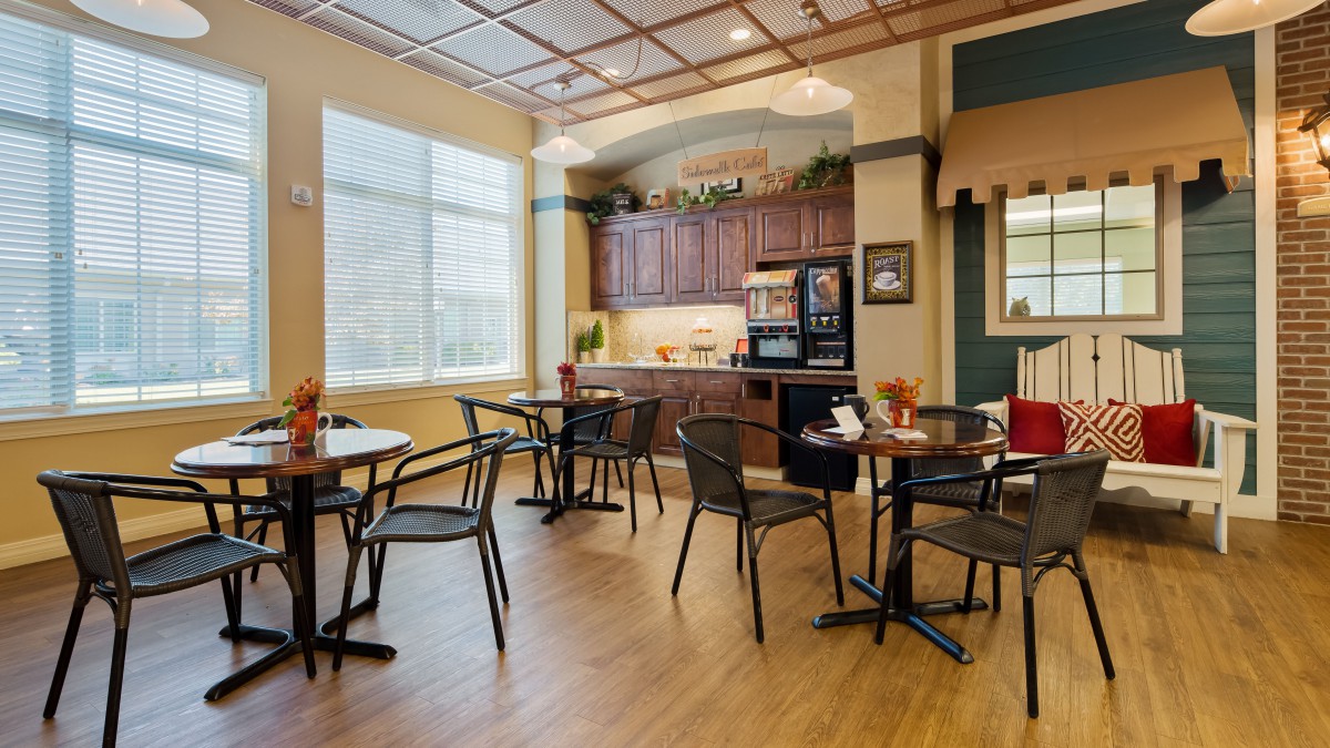 A cozy cafe interior with tables, chairs, and a kitchen area.