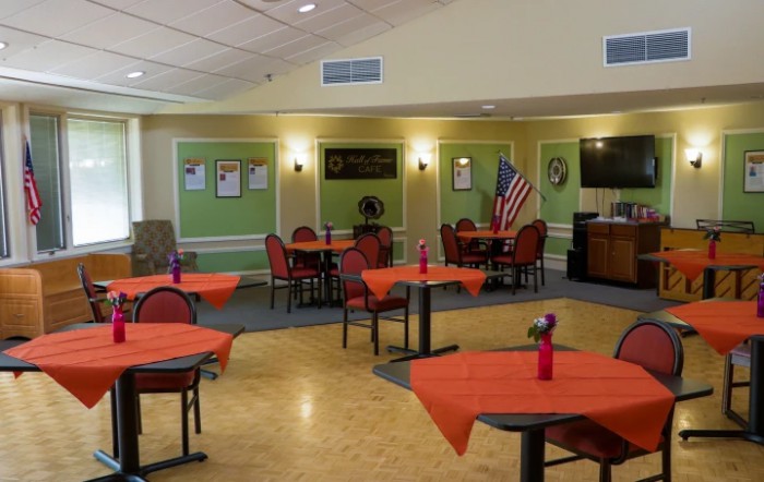 A dining area with tables covered in orange tablecloths, decorated with small vases and an American flag.