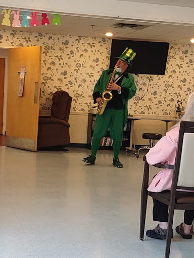 A saxophonist in a vibrant green outfit performs for an audience at a community center.