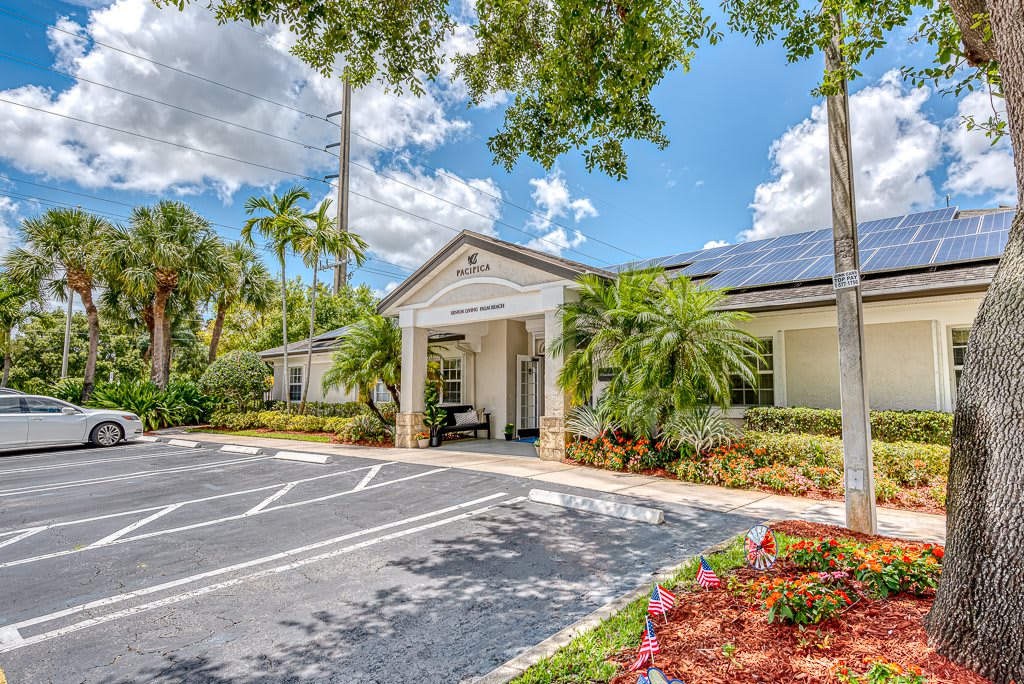 A sunny day view of a building entrance with a well-maintained parking lot and lush greenery.