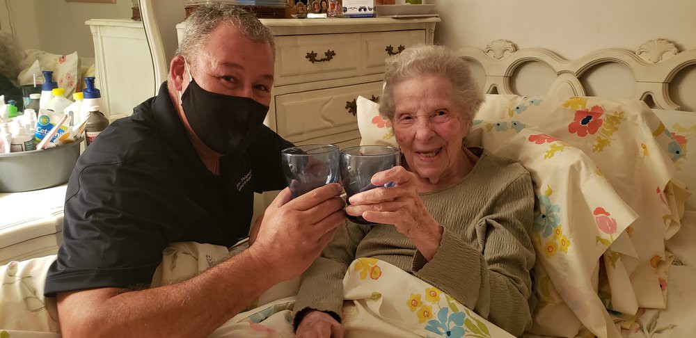 An elderly woman and a man wearing a mask are celebrating together, toasting with glasses while sitting indoors.