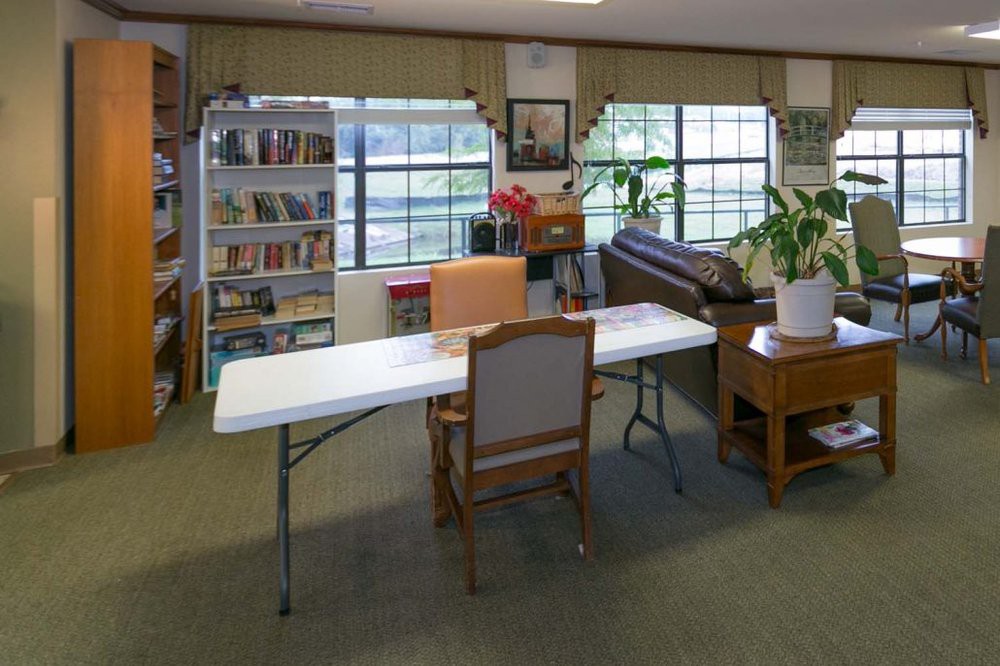 A library room with a table and chairs, bookshelves, and a plant near the windows.