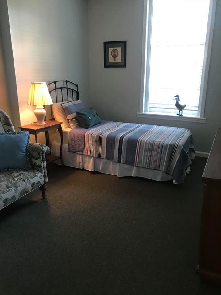 A cozy bedroom with a single bed, lamp, and armchair.