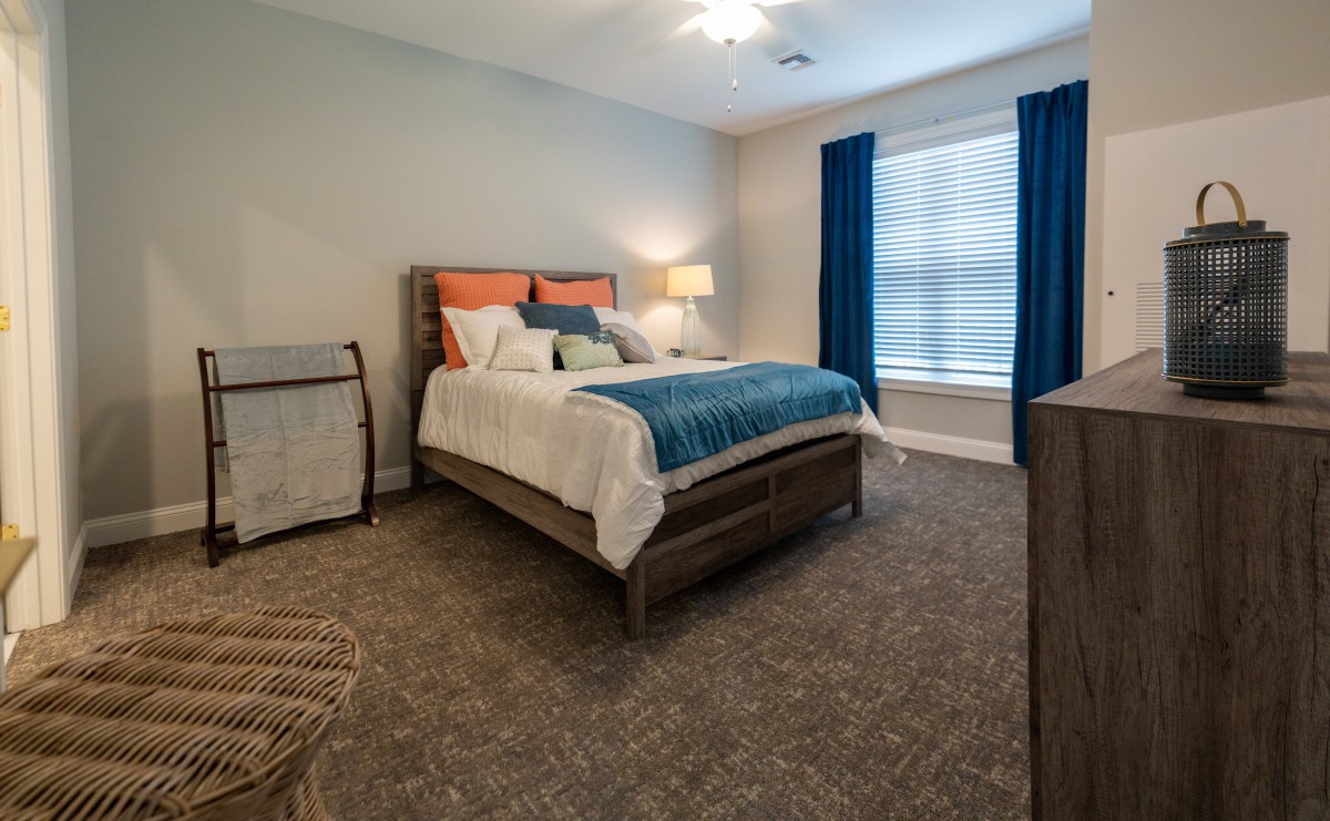 A cozy bedroom with a large bed, colorful pillows, and blue curtains.