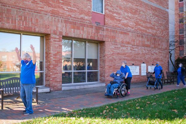 Healthcare workers assisting individuals in wheelchairs outside a brick building.