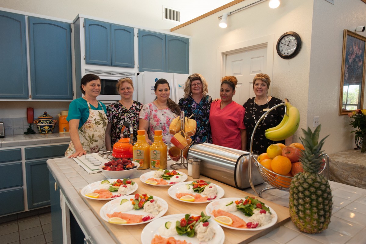 A group of women preparing a meal in a kitchen, with plates of food and various fruits on display.