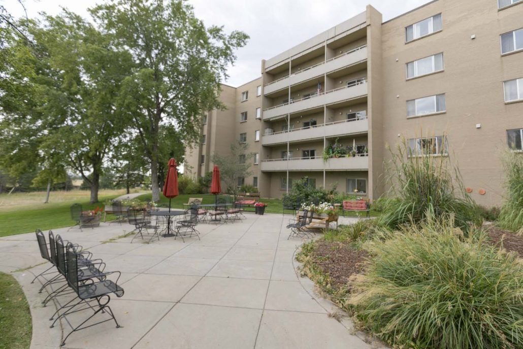 An apartment building with a landscaped outdoor patio area featuring tables and chairs.