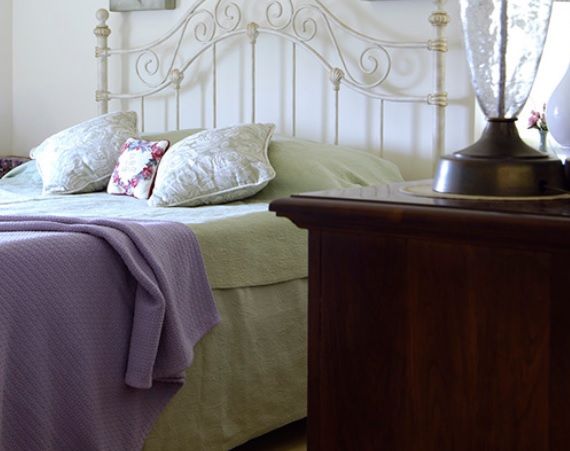 A cozy bedroom with an ornate metal headboard, plush pillows, and a small bedside table with a lamp.