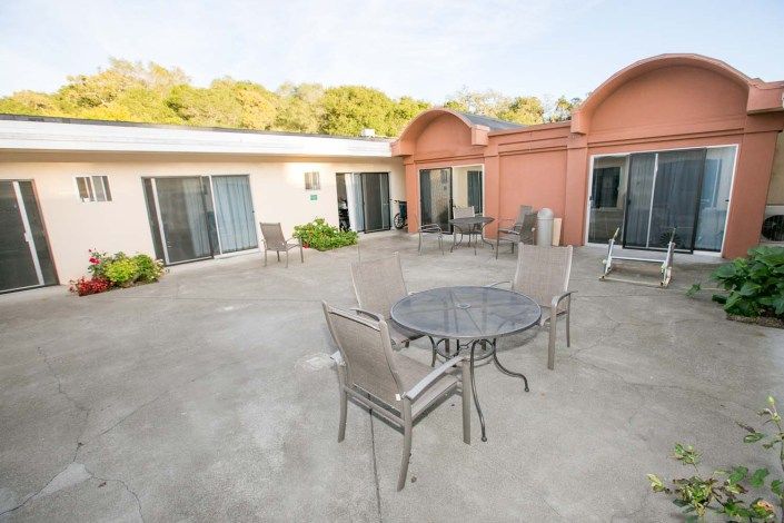 A spacious patio with outdoor furniture, including a table and chairs, set in the backyard of a house featuring sliding doors.