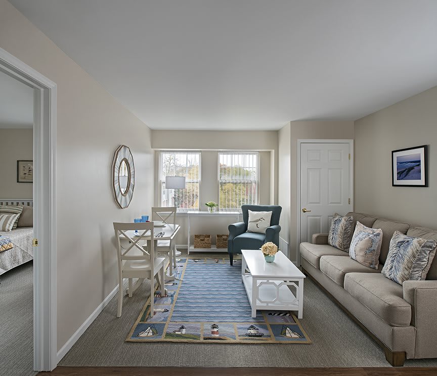 A cozy living room with a sofa, armchair, and a coffee table beside a large window.