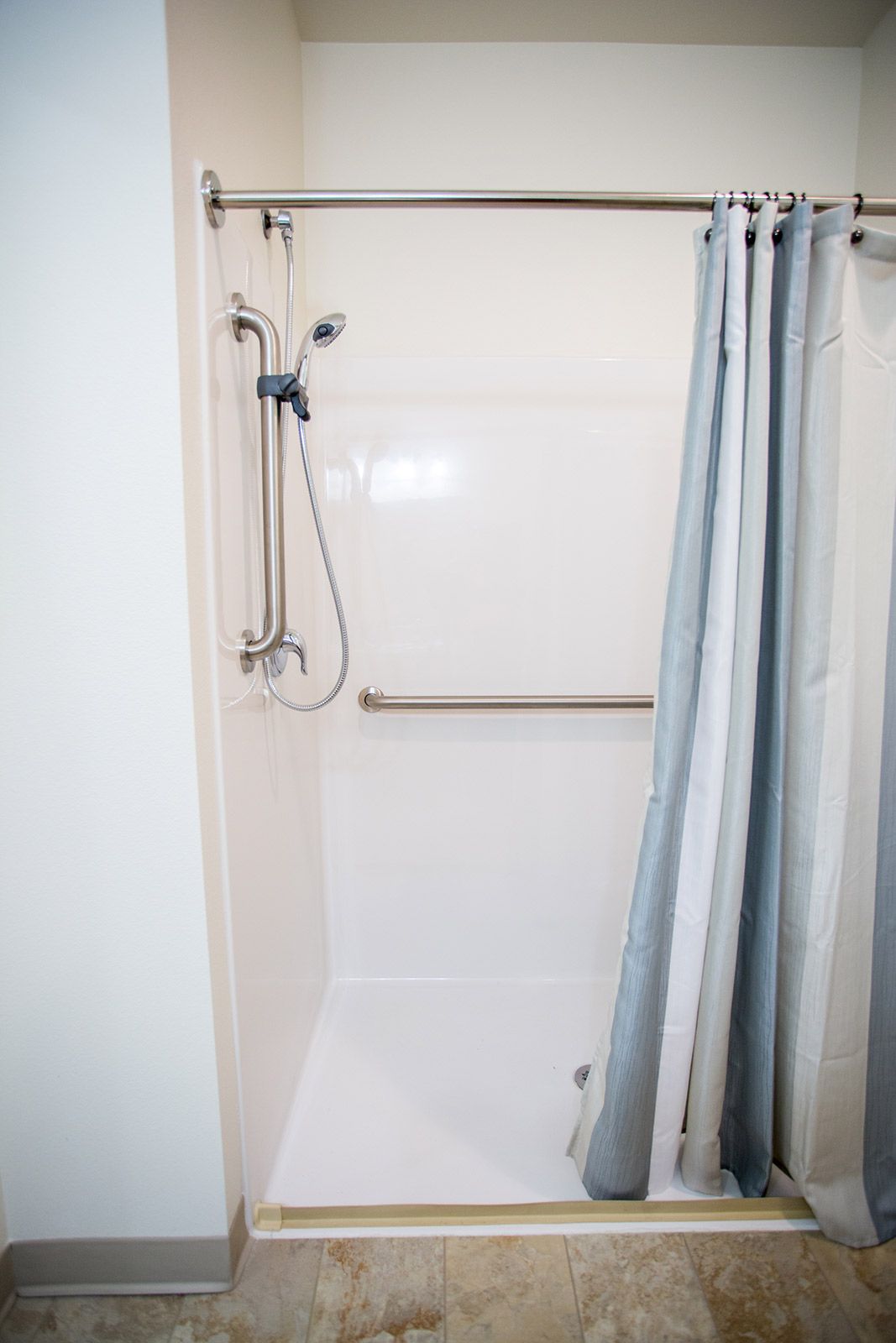 A clean, accessible shower with a handheld shower head and grab bar.