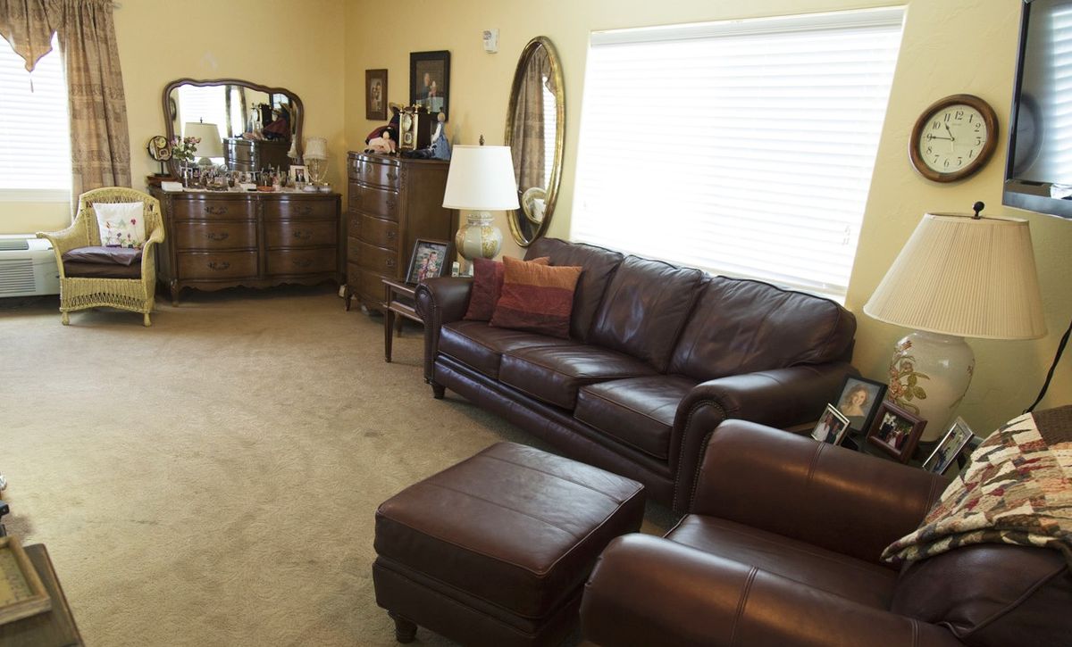 A cozy living room featuring a leather sofa and matching armchair, with wooden furniture and a large window providing natural light.