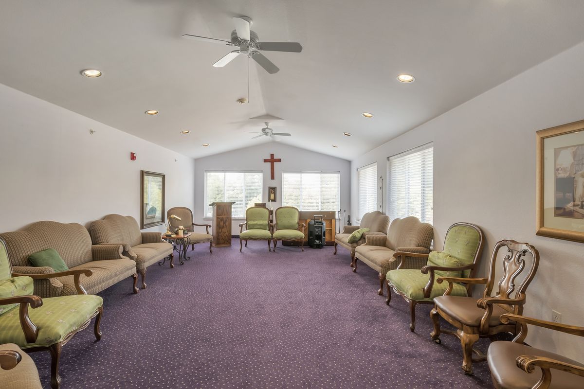 A spacious meeting room with seating arranged in a circle, featuring a cross on the wall and ceiling fans overhead.