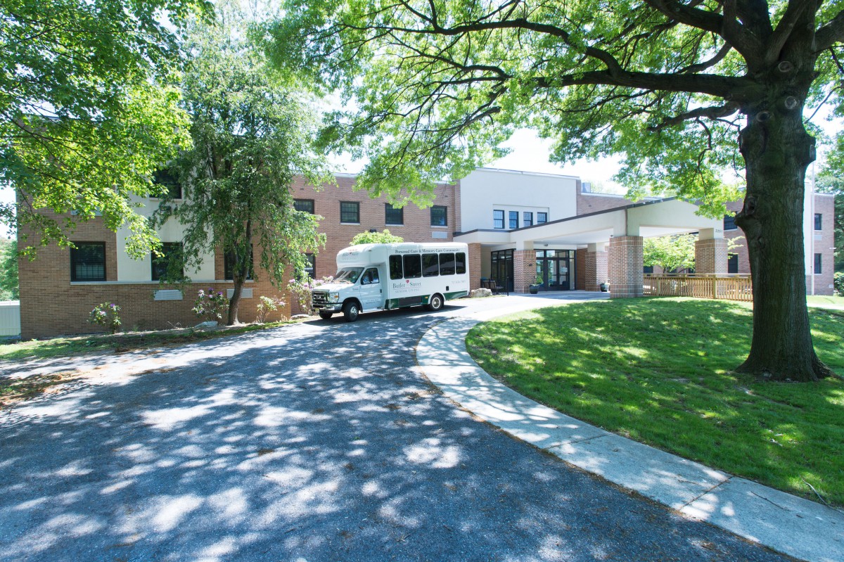 A building with a driveway and a bus parked under the shade of trees.