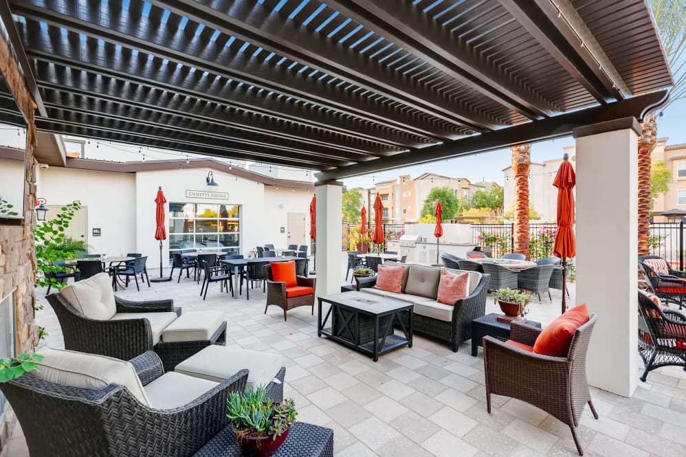 A modern outdoor patio with comfortable seating under a pergola, featuring tables and red umbrellas.