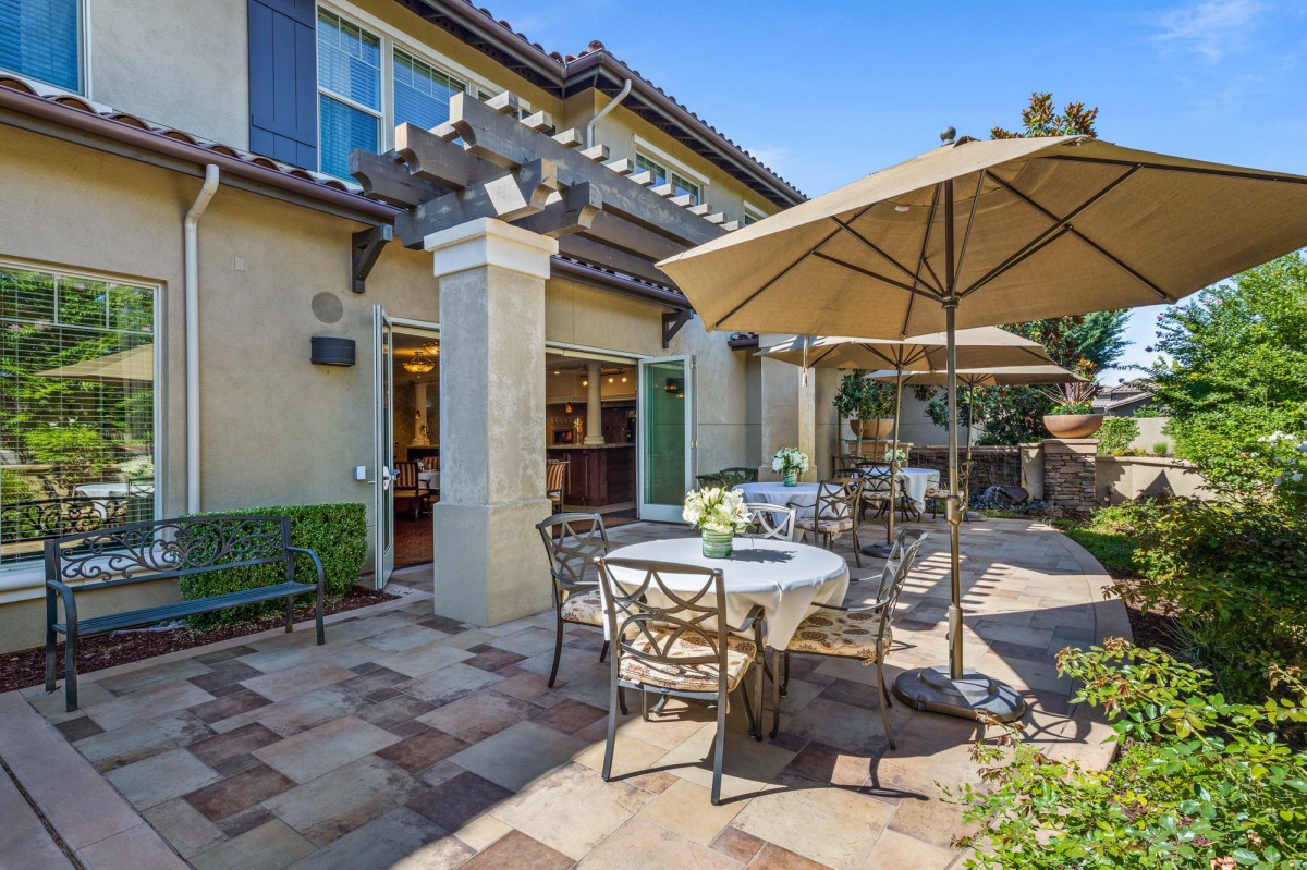 A charming patio area with tables, chairs, and umbrellas outside a residential home on a sunny day.