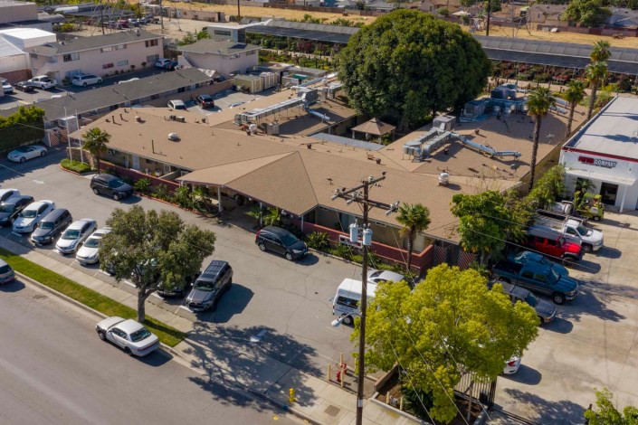 Aerial view of a suburban area with a building and parking lot surrounded by trees and parked cars.