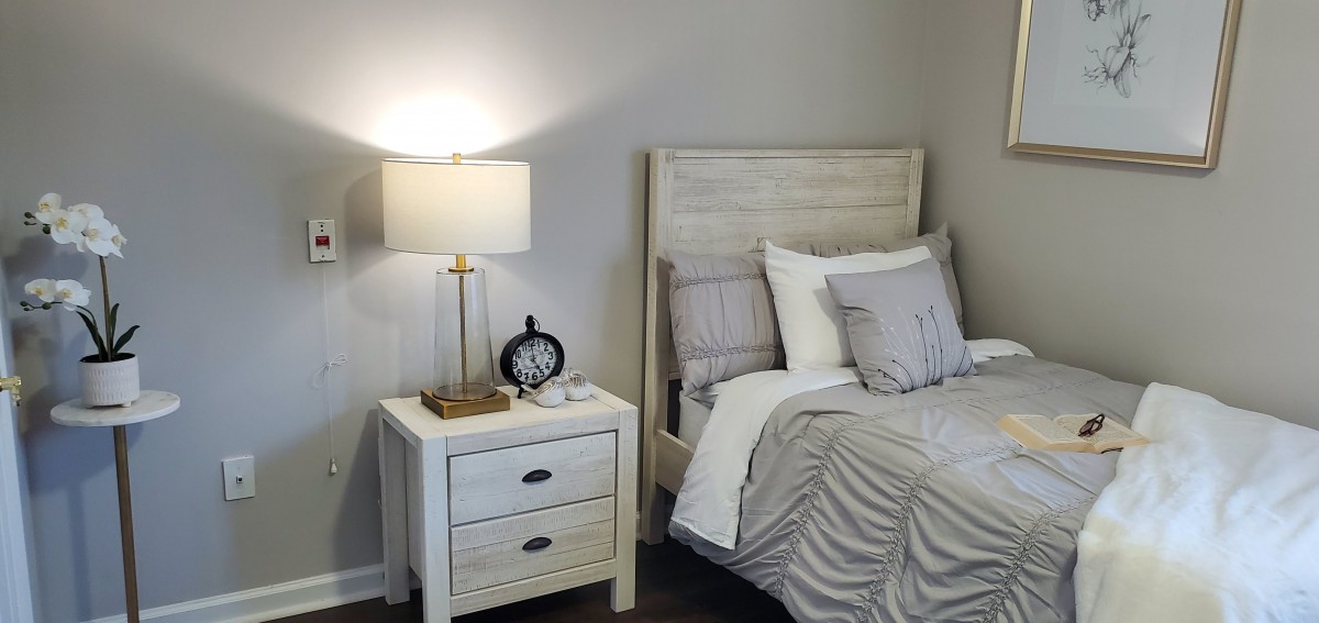 A cozy bedroom with a neatly made bed, nightstand with a lamp, and a decorative clock.