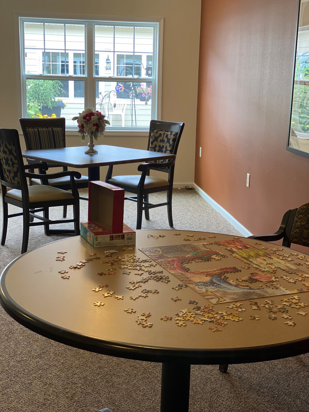 A cozy room featuring a table with an incomplete puzzle and a dining set by the window.