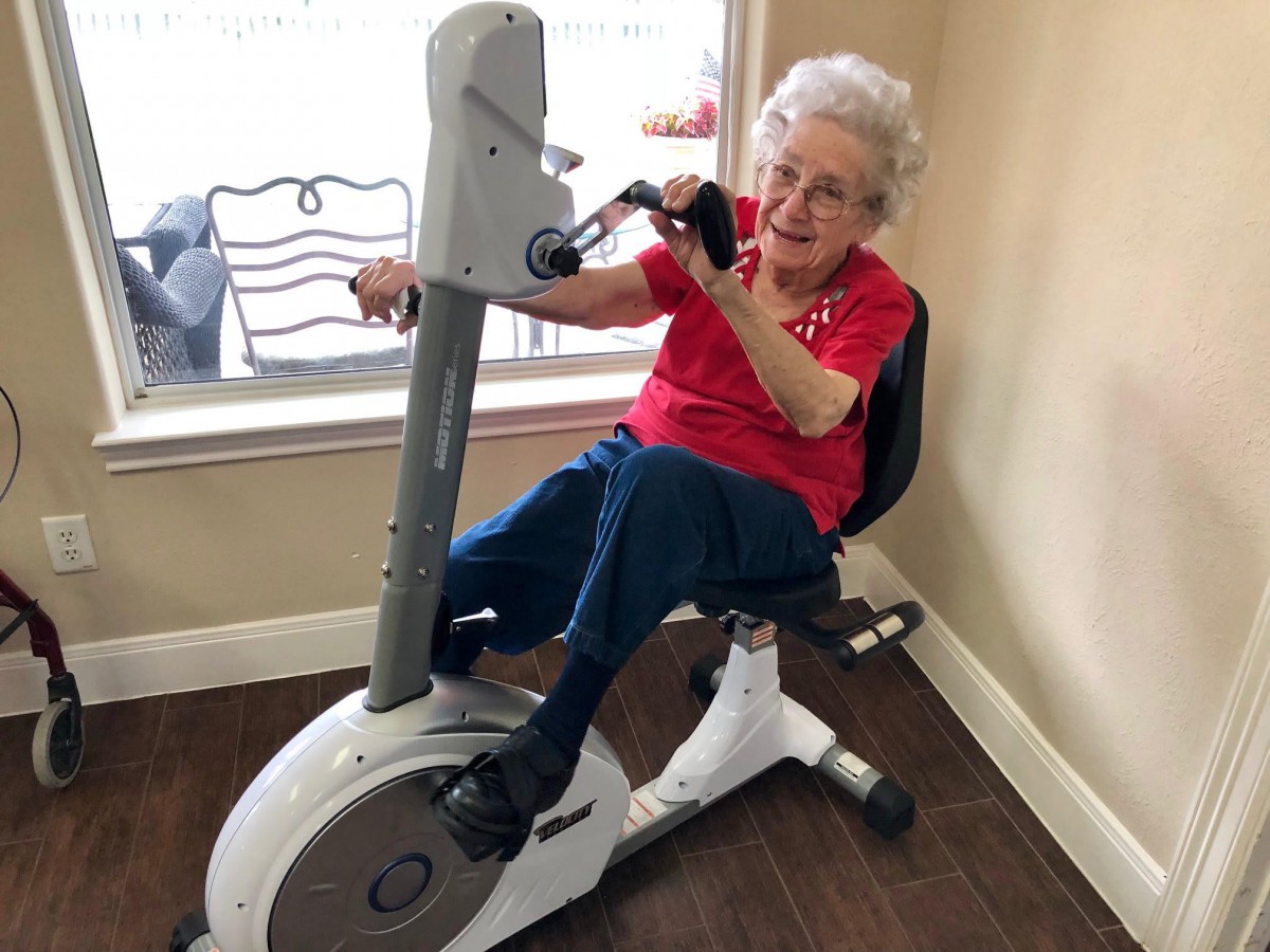 An elderly woman using an exercise bike indoors.