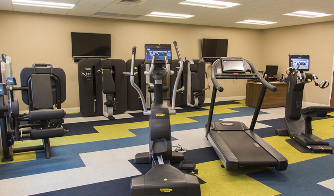A modern gym featuring various exercise machines including a treadmill and an elliptical.