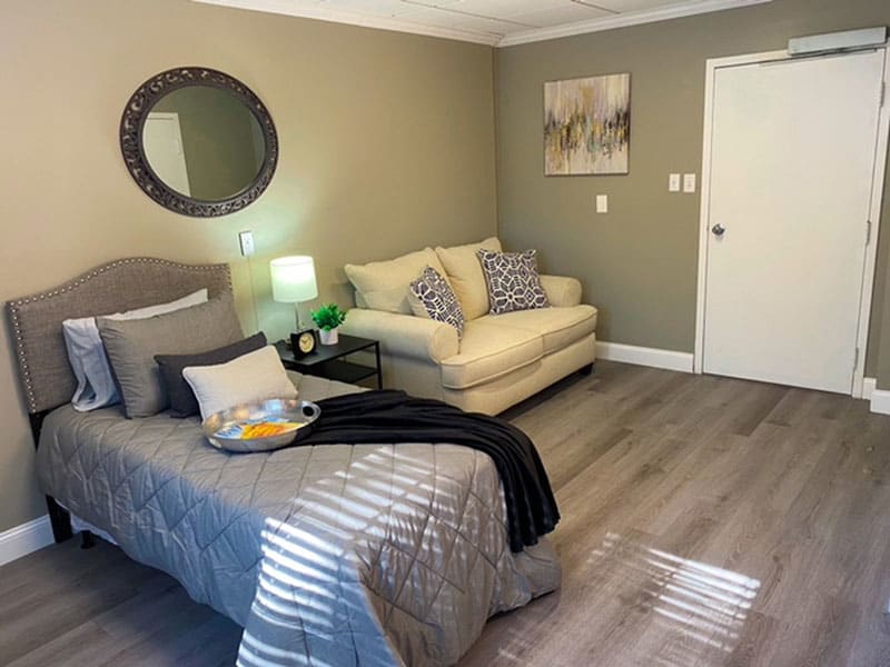A cozy bedroom with a stylish bed and a comfortable sofa, complemented by decorative items like a mirror and artwork.