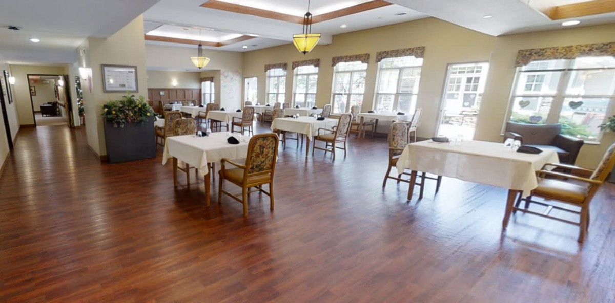A spacious dining room with neatly arranged tables and chairs, accented by large windows.