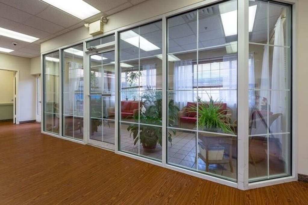 An office lobby with glass walls, featuring comfortable seating and indoor plants.