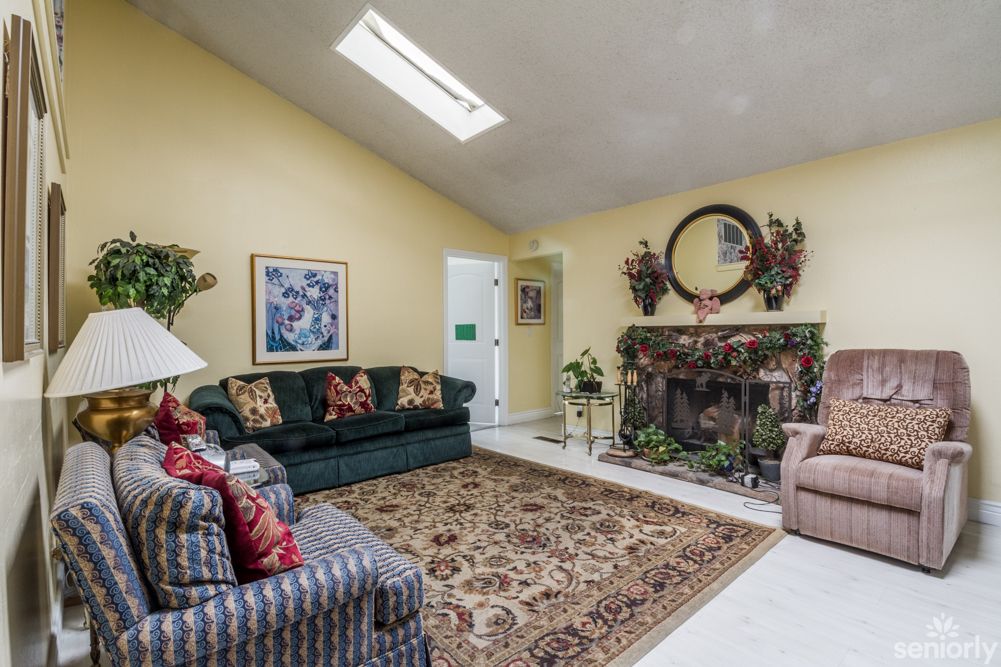 A cozy living room featuring a fireplace, colorful sofas, and a patterned carpet beneath a skylight.