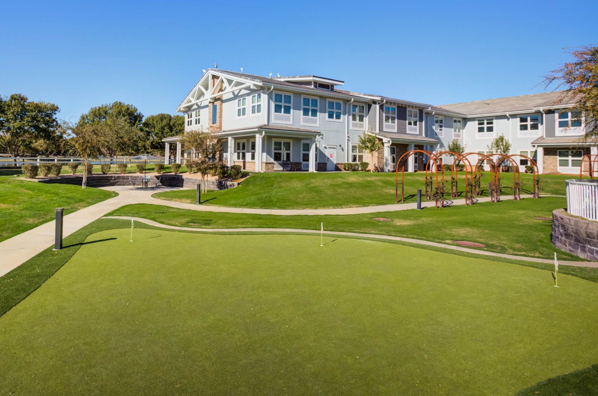 A clubhouse overlooking a green golf course under a clear blue sky.