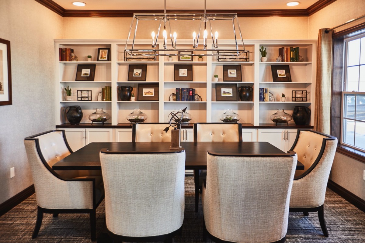 A stylish dining room with a modern chandelier and bookshelves in the background.