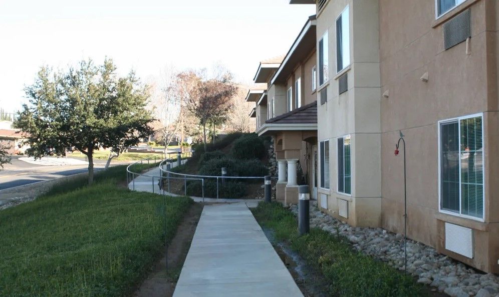 A sidewalk leads to a building surrounded by trees and grass.