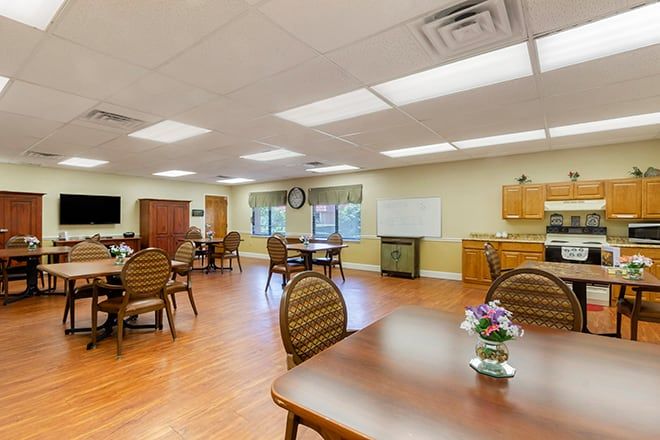 A well-lit dining area in a senior living facility with multiple tables and chairs.