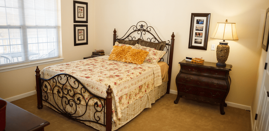 A cozy bedroom with a decorative iron bed frame, floral quilt, and accent pillows, complemented by framed pictures on the walls.