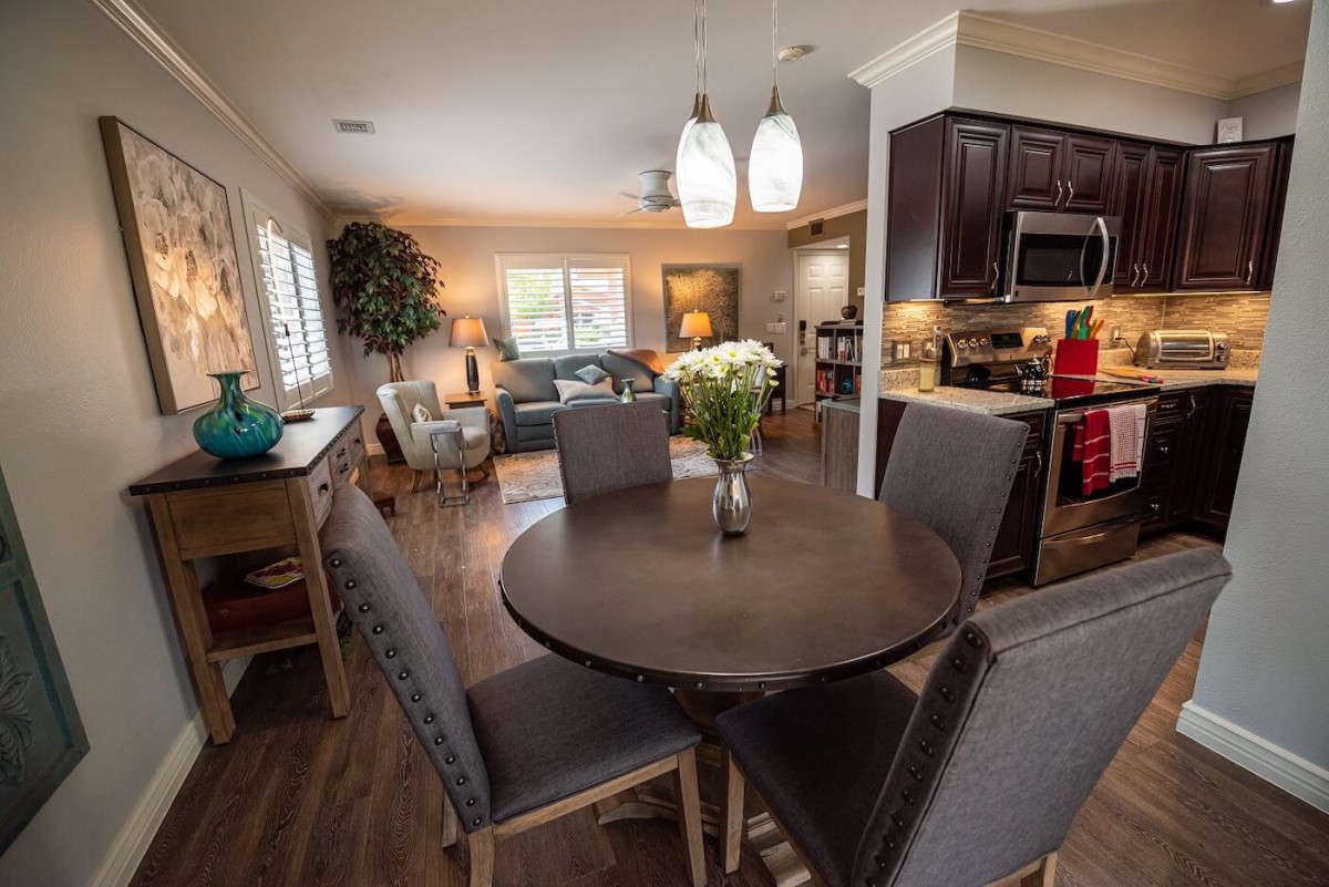A modern open-concept living space featuring a dining area with a round table and upholstered chairs, adjacent to a kitchen with dark cabinetry.
