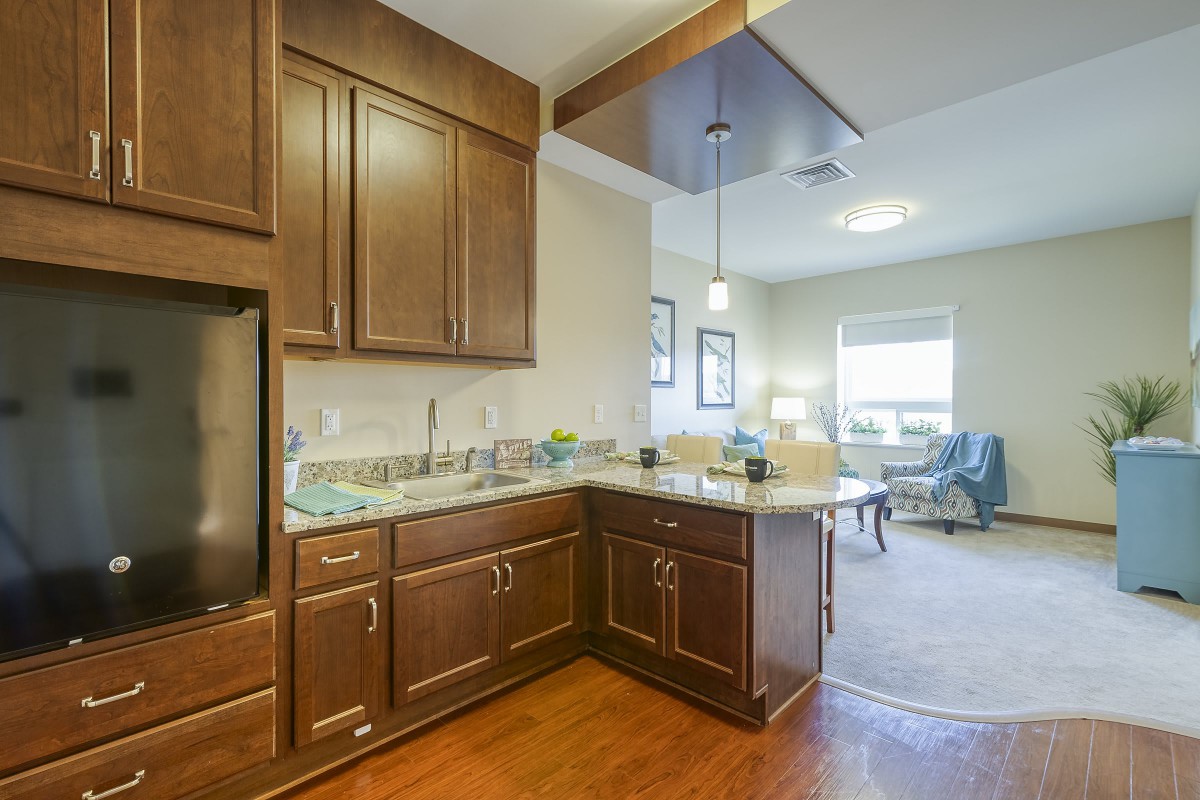 A modern kitchen with wooden cabinets and an open layout leading to a living area.