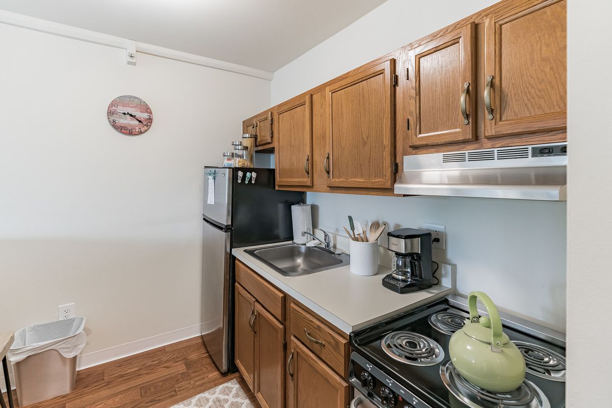 A compact kitchen with wooden cabinets, a refrigerator, stove, and countertop appliances.